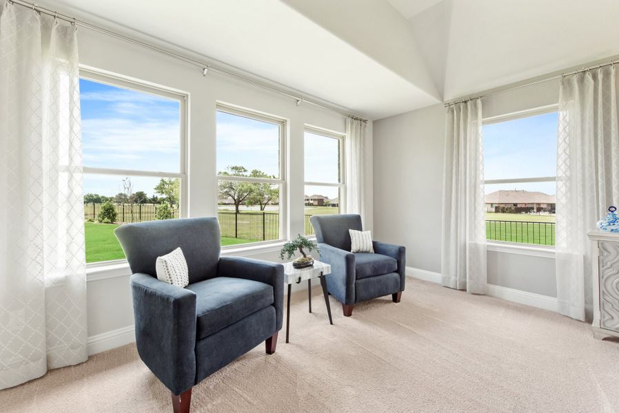 Sitting area with two blue armchairs, carpet flooring, and large windows overlooking a backyard