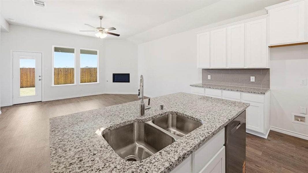 Kitchen featuring white cabinetry, dark wood-style flooring, backsplash, stainless steel dishwasher, and light stone countertops