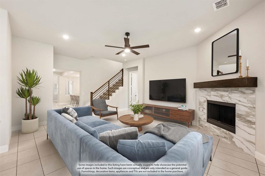 Living room with marble fireplace, ceiling fan, blue sectional sofa, and staircase with modern railing Living room with marble fireplace, ceiling fan, blue sectional sofa, and staircase with modern railing