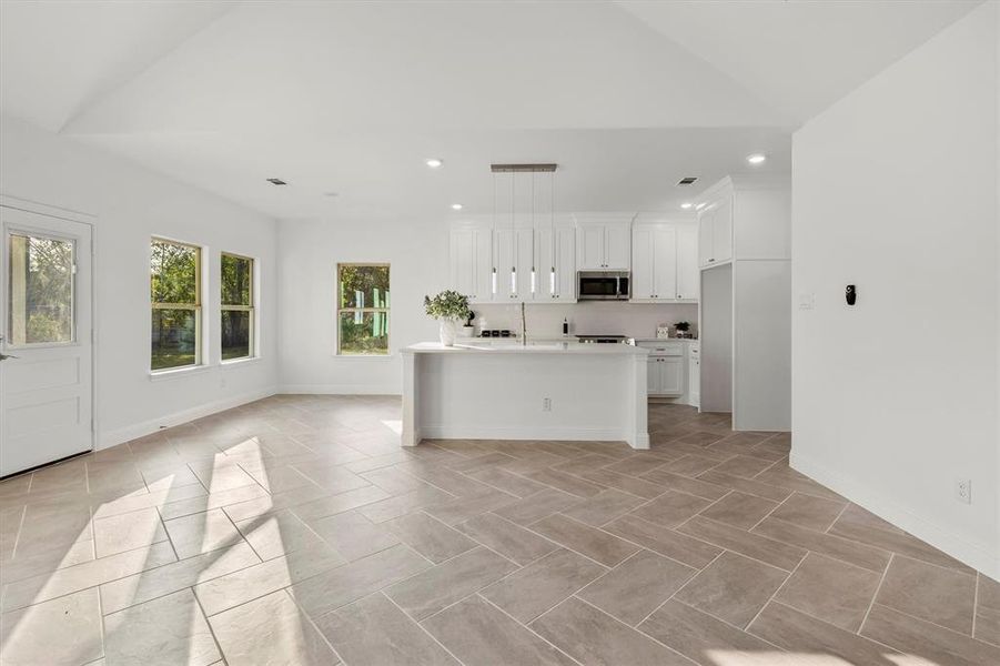 Kitchen featuring lofted ceiling, white cabinetry, a kitchen island with sink, and pendant lighting