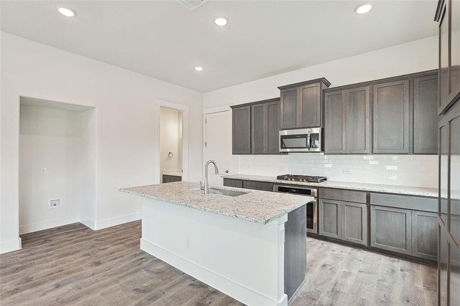 Kitchen with appliances with stainless steel finishes, tasteful backsplash, sink, a kitchen island with sink, and light stone counters