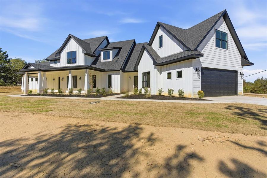 Modern farmhouse with board and batten siding, a porch, concrete driveway, and a shingled roof Modern farmhouse with board and batten siding, a porch, concrete driveway, and a shingled roof