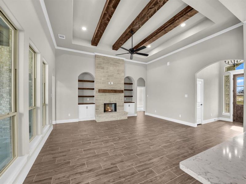 Unfurnished living room with wood tiled floors, a fireplace, beamed ceiling, a raised ceiling, and recessed lighting Unfurnished living room with wood tiled floors, a fireplace, beamed ceiling, a raised ceiling, and recessed lighting