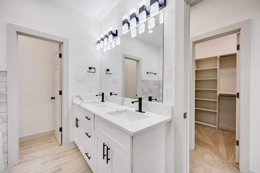 Elegant primary bathroom with dual sinks, quartz countertops, shaker-style cabinetry, matte black fixtures, and a full-length mirror with modern lighting.
