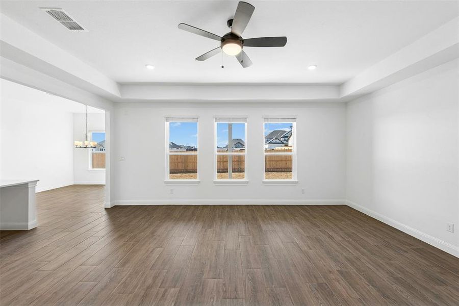 Spacious interior room featuring wood-finish flooring, a tray ceiling, and a modern ceiling fan with integrated lighting
