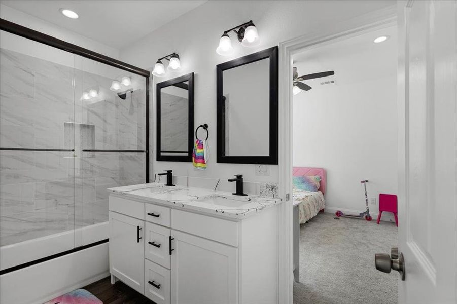 Full bath featuring connected bathroom, double vanity, bath / shower combo with glass door, recessed lighting, and dark carpet Full bath featuring connected bathroom, double vanity, bath / shower combo with glass door, recessed lighting, and dark carpet