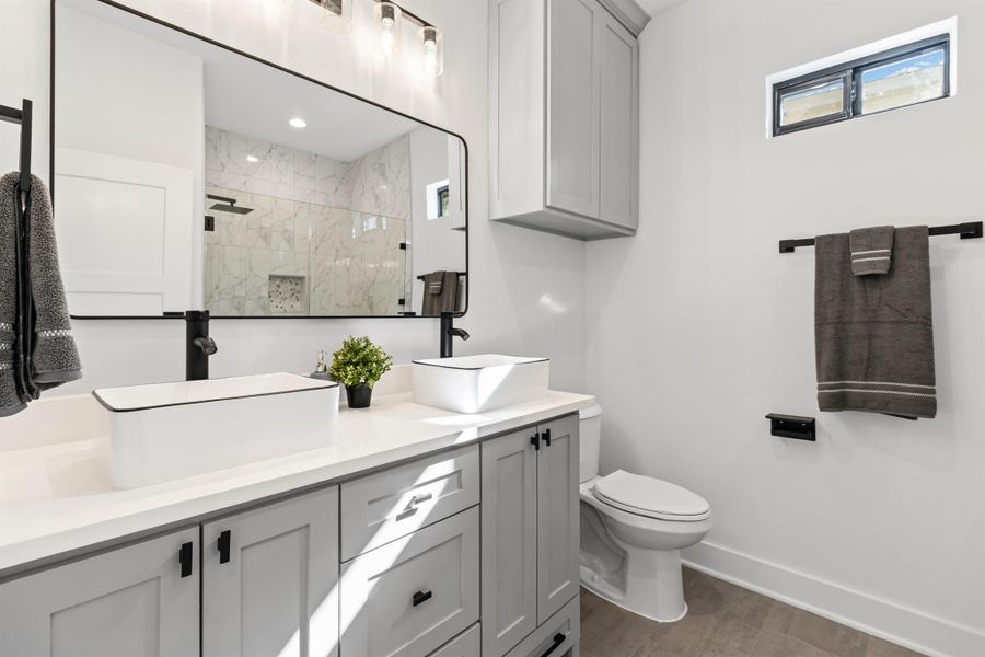 Bathroom featuring double vanity, tiled shower, and dark wood-style floors