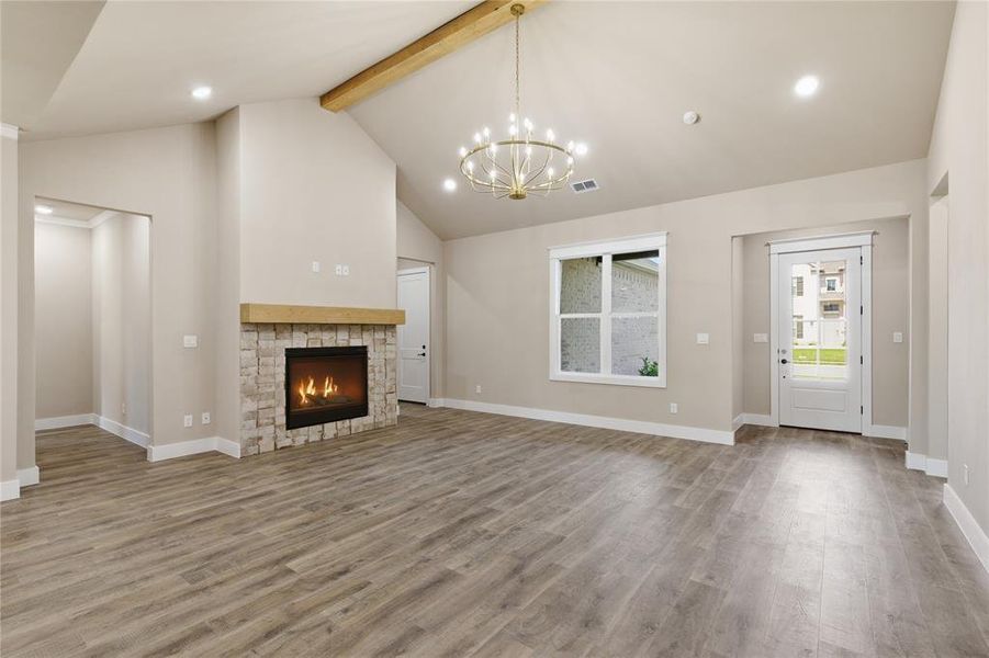 Vaulted ceiling main living area featuring a stone fireplace with wood mantel, wood-finish flooring, and a contemporary chandelier