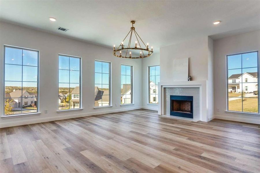 Unfurnished living room with light wood finished floors, recessed lighting, a brick fireplace, a chandelier, and a residential view