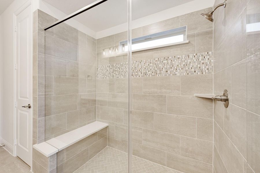 Walk-in shower with glass door, beige tile walls, mosaic accent strip, built-in bench, and overhead window Walk-in shower with glass door, beige tile walls, mosaic accent strip, built-in bench, and overhead window