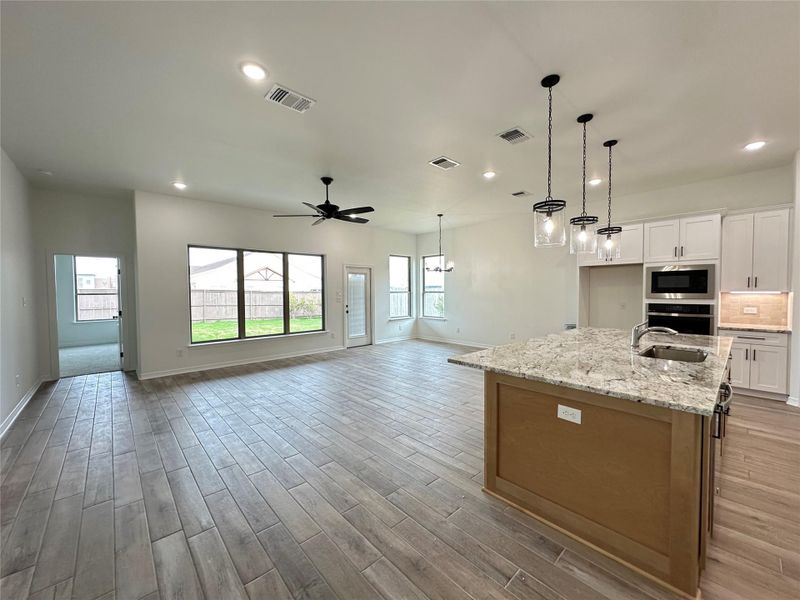 Kitchen with white cabinets, a center island with sink, light stone countertops, decorative light fixtures, and oven