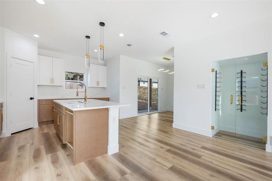 Kitchen with white cabinets, a center island with sink, sink, light wood-type flooring, and decorative light fixtures