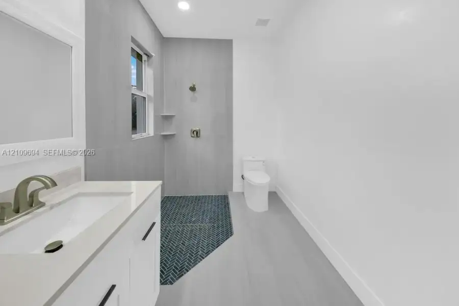 Bathroom featuring a white vanity with a stone countertop, an integrated rectangular sink, shower enclosure with floor-to-ceiling gray tile, herringbone-patterned shower floor, and a dual-flush toilet