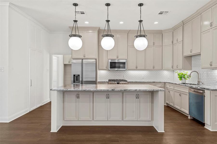Kitchen featuring stainless steel appliances, a kitchen island, decorative backsplash, dark wood-type flooring, and light stone countertops Kitchen featuring stainless steel appliances, a kitchen island, decorative backsplash, dark wood-type flooring, and light stone countertops