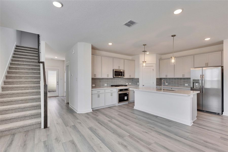 Kitchen featuring appliances with stainless steel finishes, a kitchen island with sink, pendant lighting, backsplash, and recessed lighting