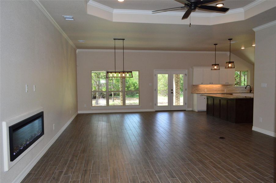 Unfurnished living room featuring a ceiling fan, crown molding, dark wood-style flooring, a tray ceiling, and a glass covered fireplace
