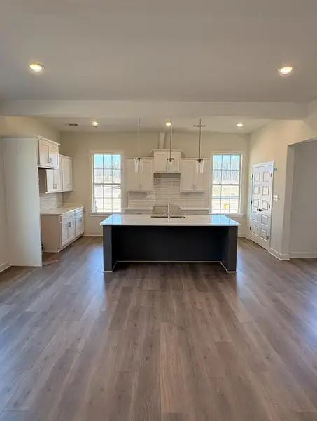 Kitchen with backsplash, white cabinetry, a center island with sink, dark wood-type flooring, and healthy amount of natural light