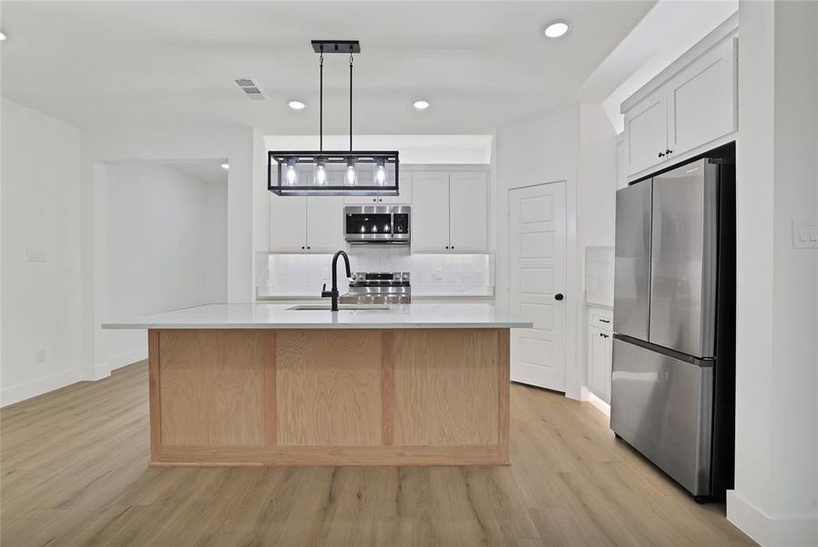 Kitchen with pendant lighting, white cabinetry, stainless steel appliances, and an island with sink.