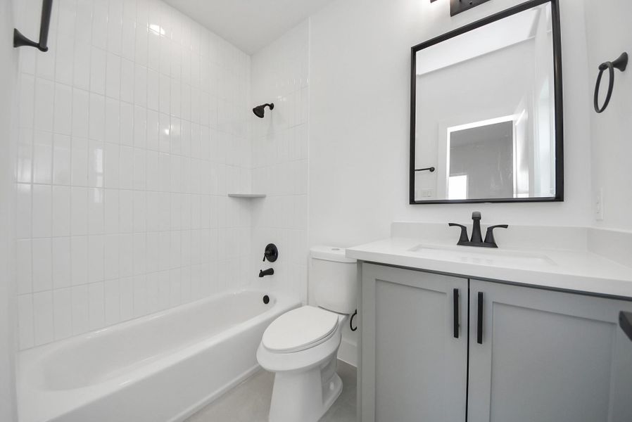 The main bathroom offers a clean, modern design with a white tiled shower, a bathtub, and a sleek vanity with large mirror. Black fixtures add contemporary elegance while the space remains bright and airy.