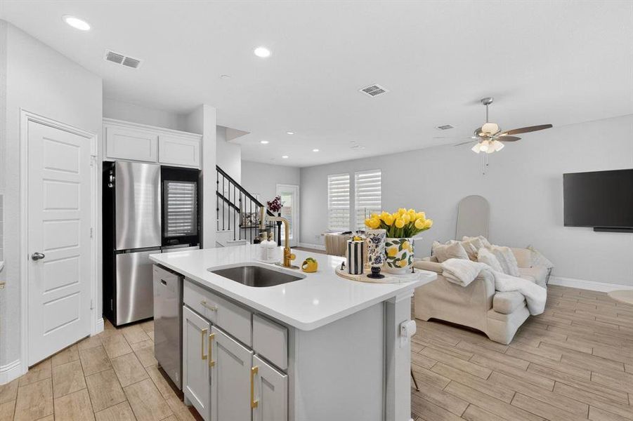 The open concept living area features light-colored flooring, a kitchen island with a sink and white countertop, and recessed lighting