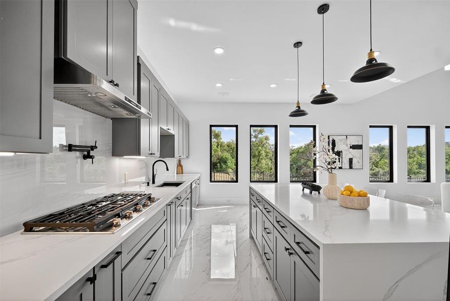 Kitchen with light stone countertops, gray cabinetry, light marble finish floors, stainless steel gas cooktop, and decorative light fixtures
