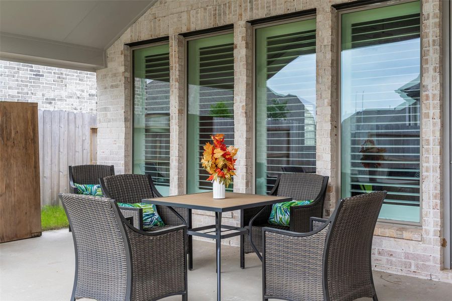 This photo showcases a cozy, covered patio with a table and four wicker chairs, perfect for outdoor dining. Large windows provide a view into the home, and a wooden fence offers privacy. This photo showcases a cozy, covered patio with a table and four wicker chairs, perfect for outdoor dining. Large windows provide a view into the home, and a wooden fence offers privacy.