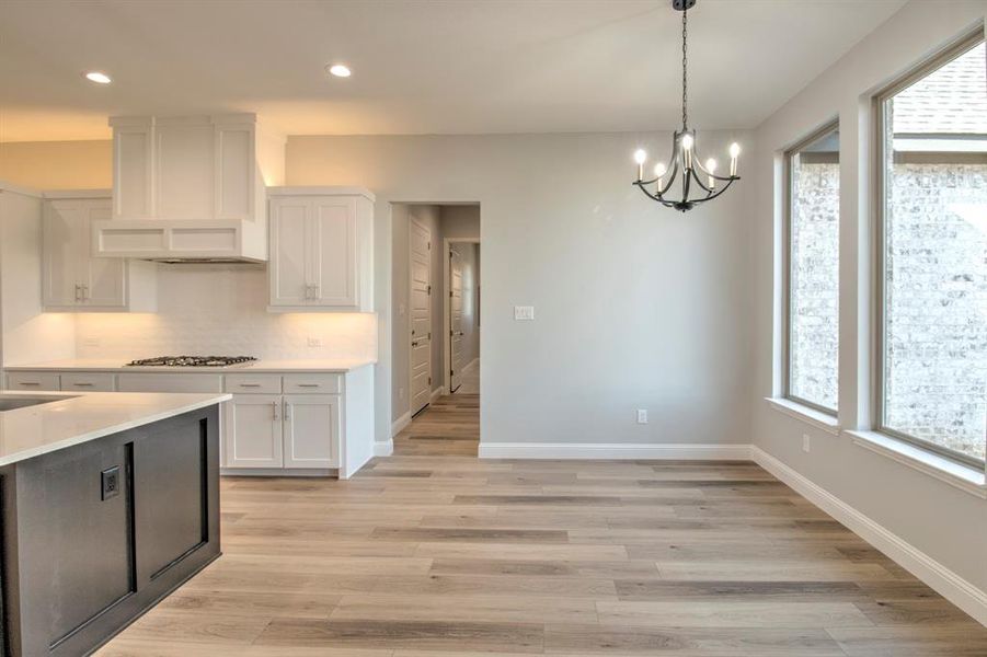 Kitchen featuring white cabinets, custom range hood, stainless steel gas cooktop, and a wealth of natural light