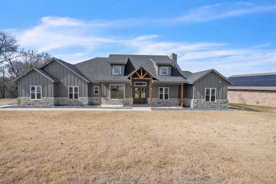 Modern inspired farmhouse featuring board and batten siding, stone siding, a porch, a chimney, and a front yard Modern inspired farmhouse featuring board and batten siding, stone siding, a porch, a chimney, and a front yard