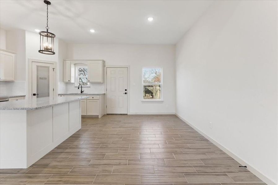 Kitchen featuring light stone counters, sink, decorative light fixtures, a notable chandelier, and white cabinetry