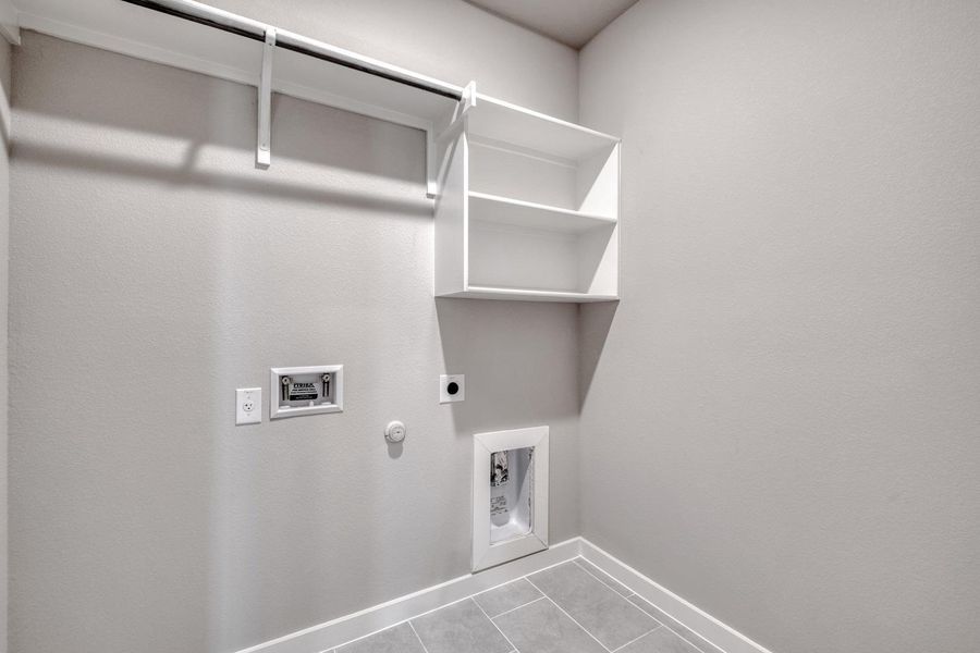 Functional laundry space featuring convenient shelving and tile flooring. Functional laundry space featuring convenient shelving and tile flooring.