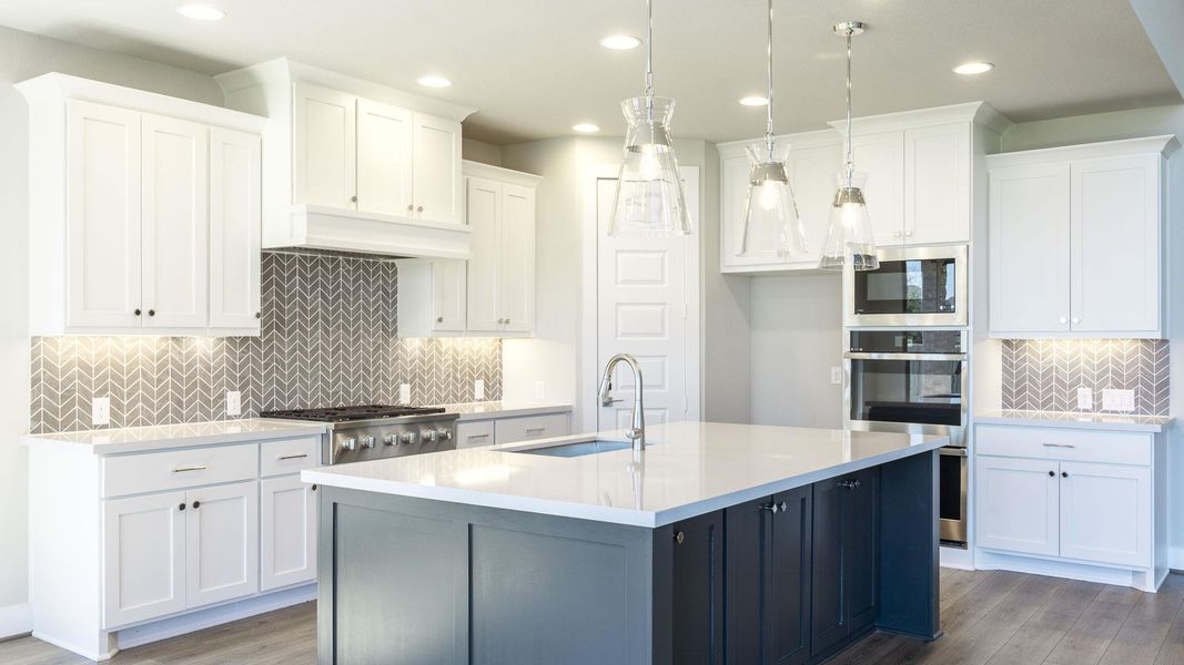 Kitchen featuring tasteful backsplash, white cabinets, light stone counters, a kitchen island with sink, and decorative light fixtures Kitchen featuring tasteful backsplash, white cabinets, light stone counters, a kitchen island with sink, and decorative light fixtures