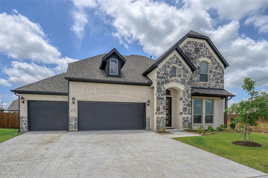 French country style house featuring stone siding, brick siding, roof with shingles, concrete driveway, and an attached garage