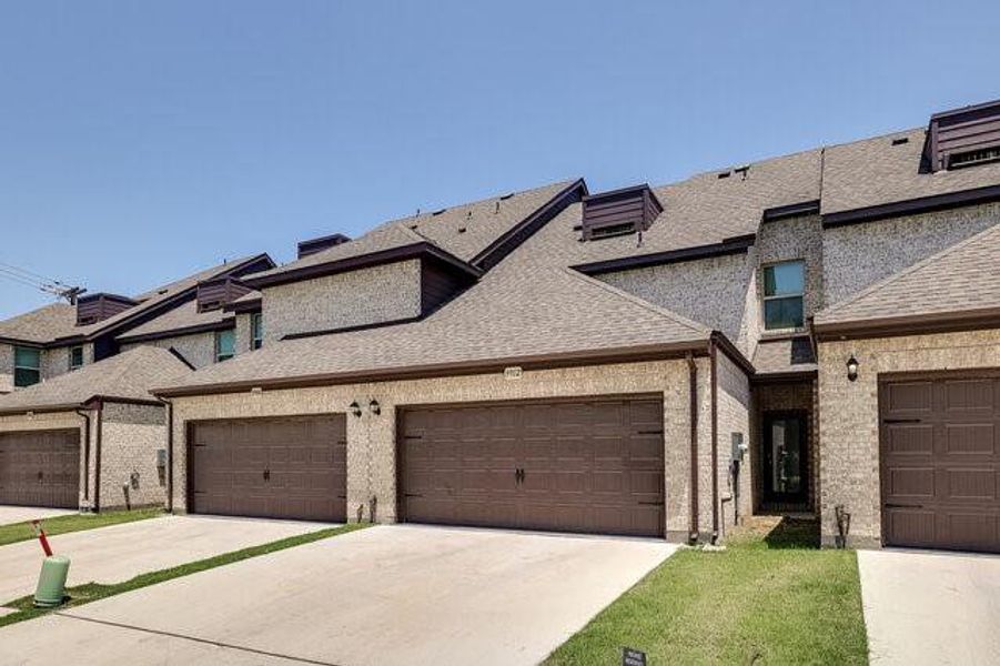 View of front of property featuring a shingled roof, driveway, and brick siding