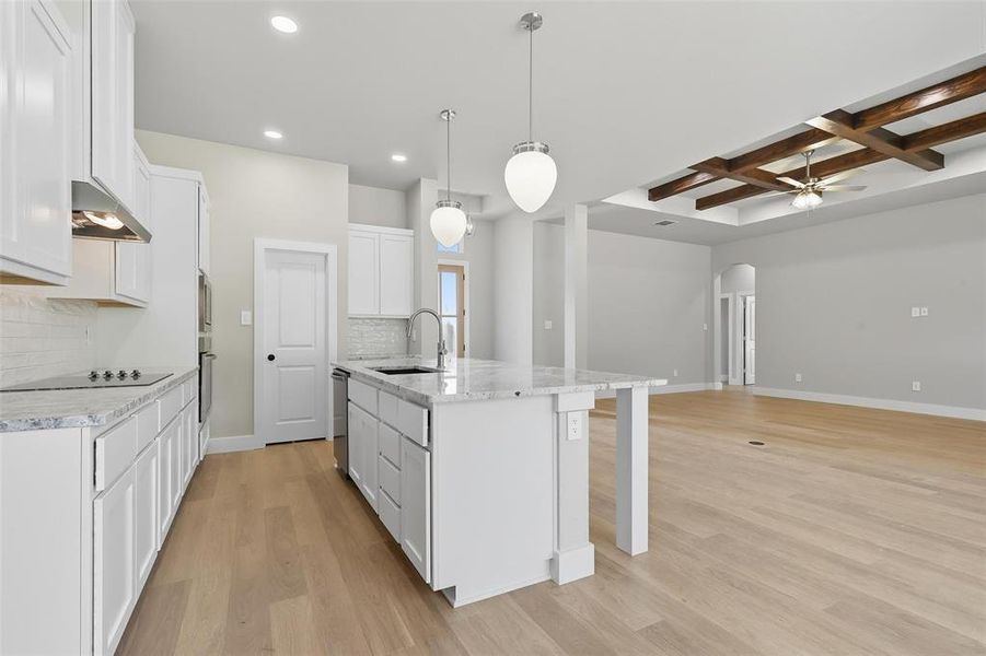 Kitchen featuring arched walkways, white cabinets, decorative backsplash, coffered ceiling, and a center island with sink