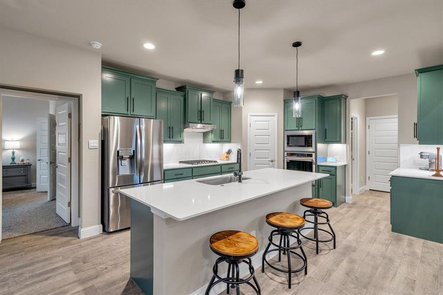 Kitchen featuring green cabinets, stainless steel appliances, a kitchen breakfast bar, decorative light fixtures, and light wood finished floors