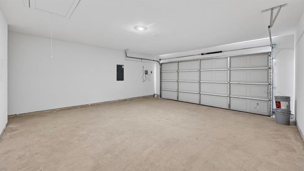 Spacious garage featuring a concrete floor, white walls, and an overhead garage door Spacious garage featuring a concrete floor, white walls, and an overhead garage door