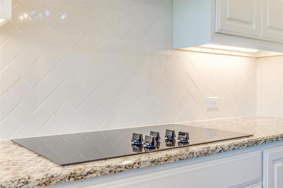 Details featuring white cabinetry, backsplash, and light stone counters