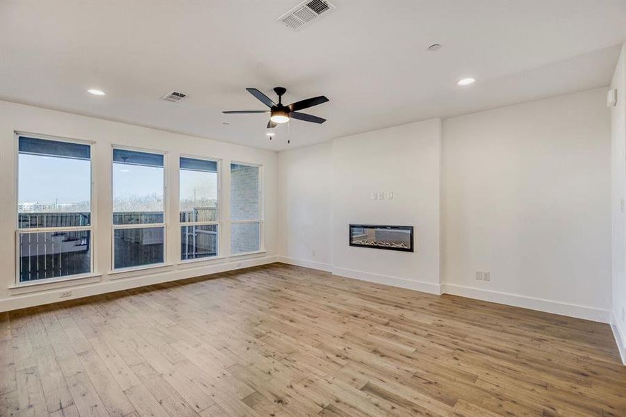 Unfurnished living room featuring light wood finished floors, a ceiling fan, a glass covered fireplace, and recessed lighting