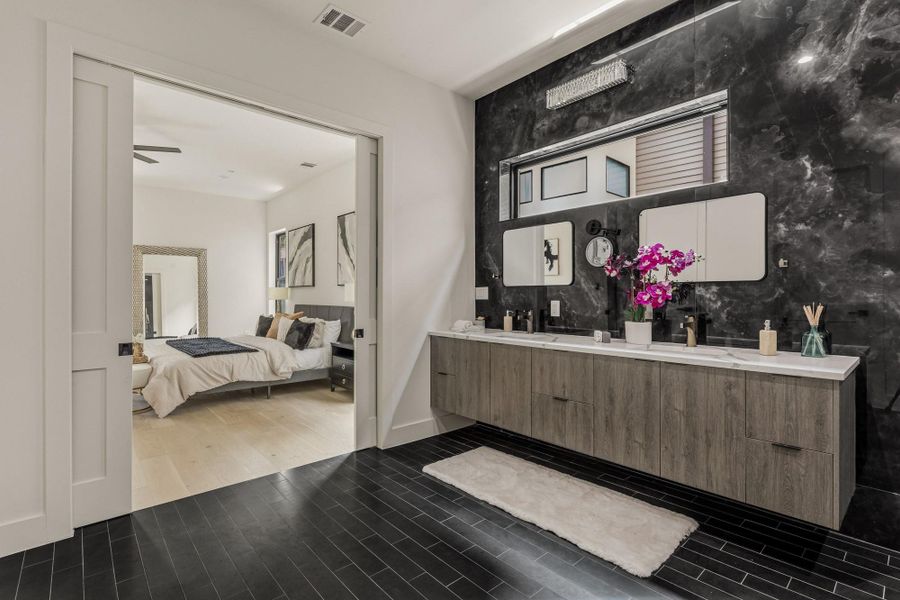Bathroom featuring a floating wood-finish vanity with a double sink, black-veined wall paneling, and dark tile flooring