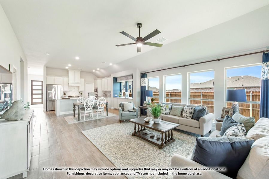 Open-concept living room with vaulted ceiling, ceiling fan, and kitchen visible in background