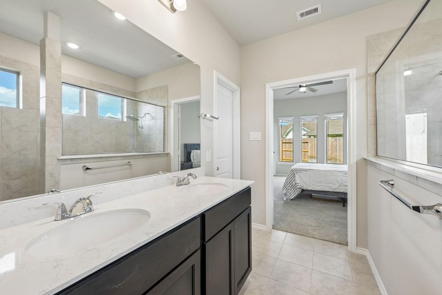 Spacious bathroom with a double vanity, large mirror, and a walk-in shower, seamlessly connected to a bright bedroom with ample natural light.