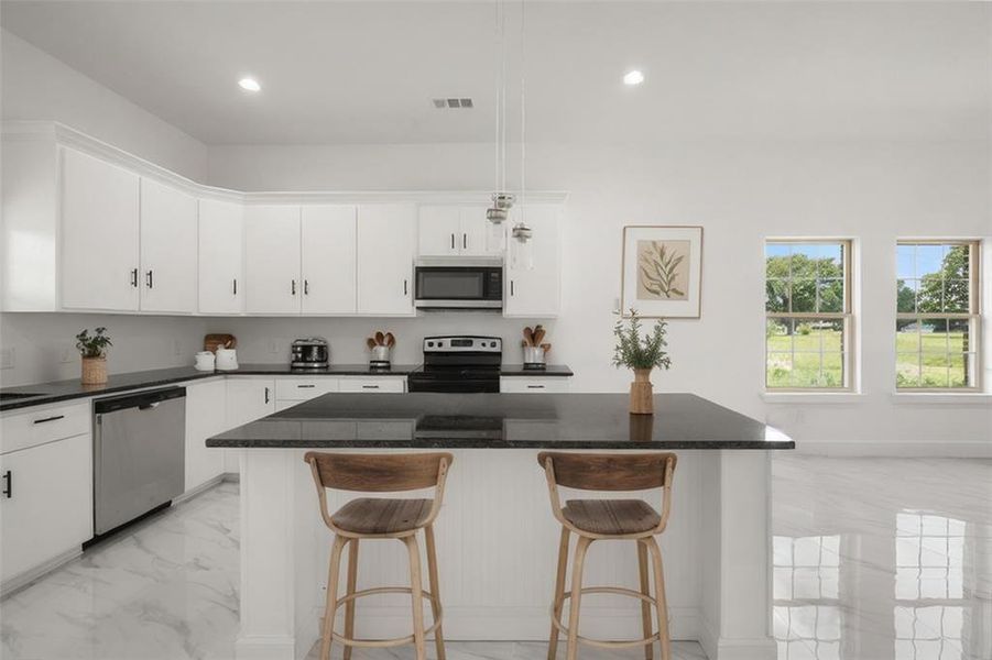 Kitchen featuring appliances with stainless steel finishes, light marble finish floors, a kitchen breakfast bar, white cabinetry, and recessed lighting Kitchen featuring appliances with stainless steel finishes, light marble finish floors, a kitchen breakfast bar, white cabinetry, and recessed lighting