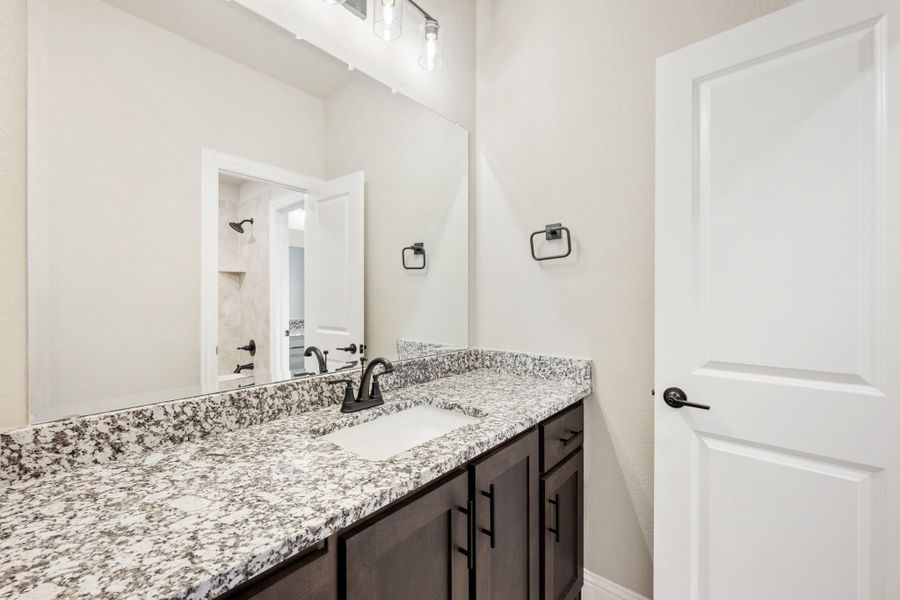 Bathroom vanity with granite countertop, dark wood cabinets, and black fixtures with large mirror above