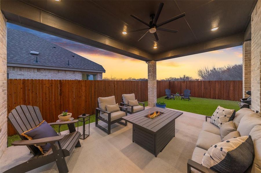 Patio terrace at dusk with a yard, an outdoor living space with a fire pit, ceiling fan, and a fenced backyard