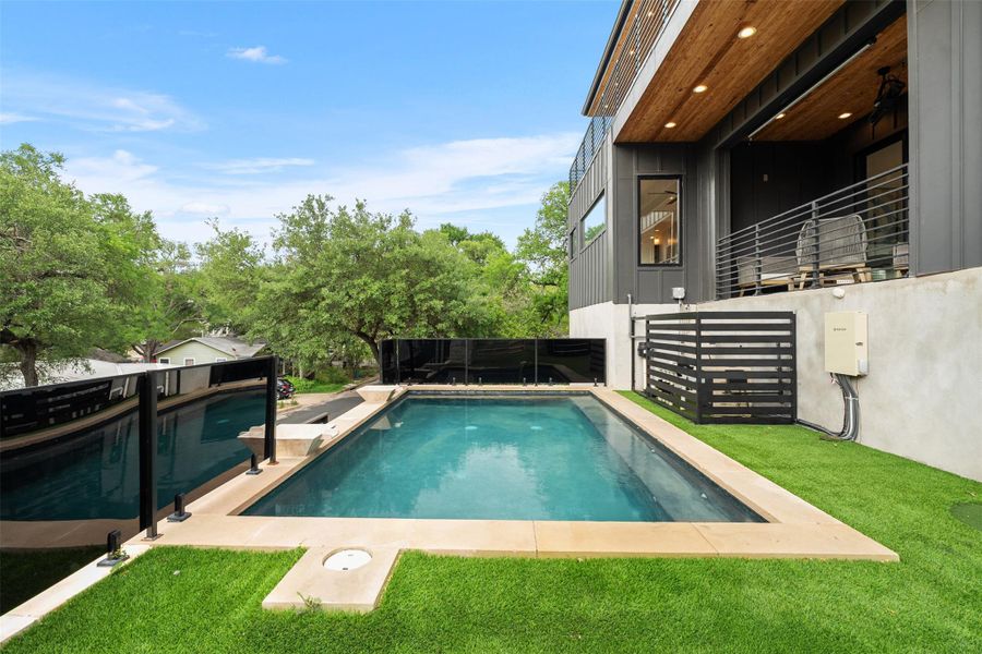 The property features a rectangular swimming pool and a separate, curved pool, both surrounded by a stone deck and artificial turf