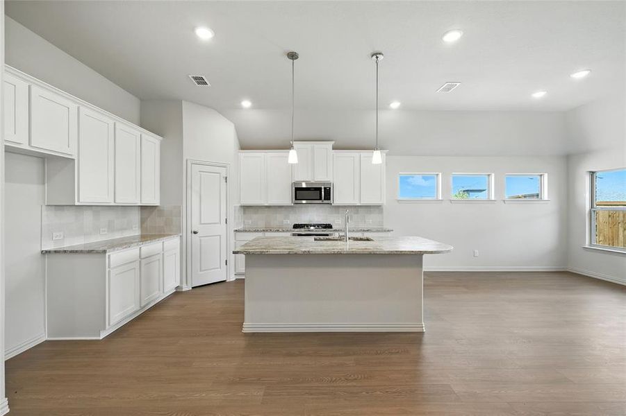 Kitchen featuring backsplash, white cabinets, light stone countertops, a kitchen island with sink, and dark wood-style floors Kitchen featuring backsplash, white cabinets, light stone countertops, a kitchen island with sink, and dark wood-style floors