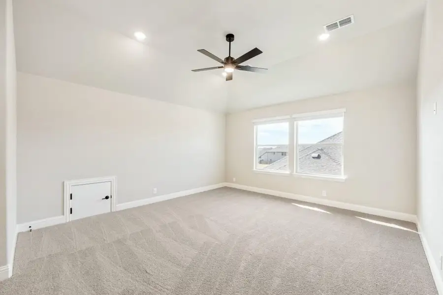 Empty bedroom with vaulted ceiling, ceiling fan, carpet flooring, and a window with natural light