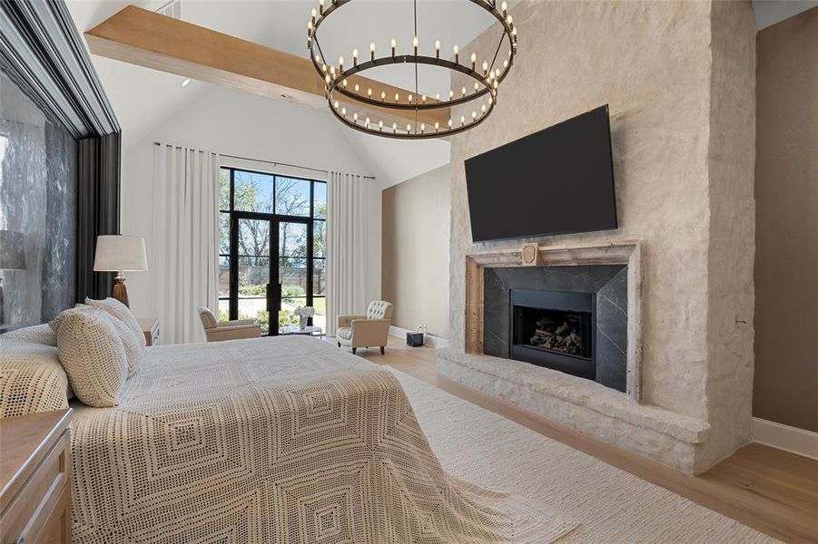 Bedroom with light wood finished floors, a high end fireplace, high vaulted ceiling, and a chandelier