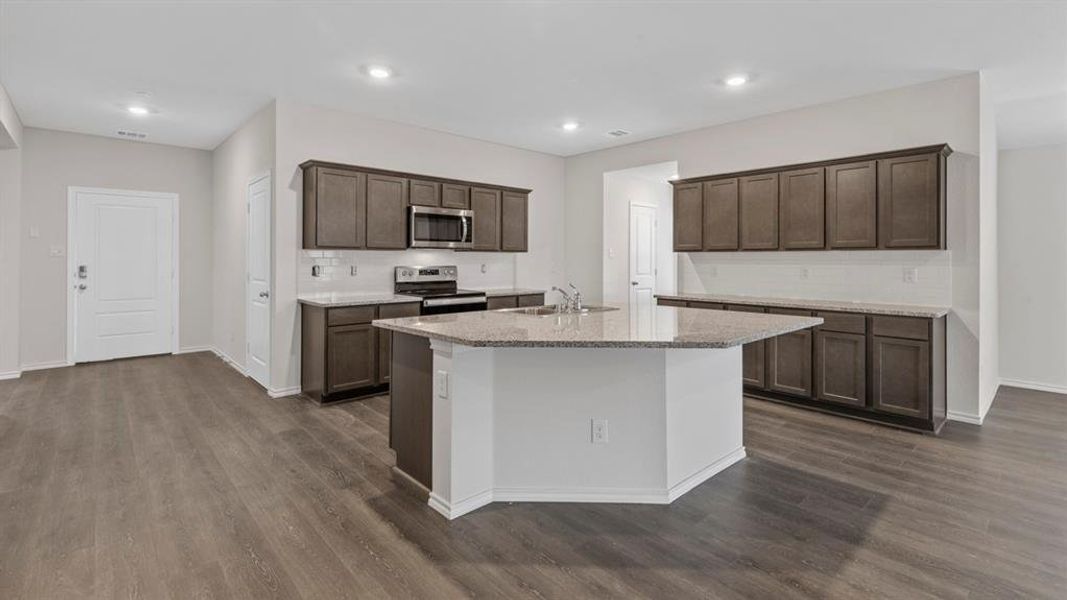 Kitchen featuring decorative backsplash, appliances with stainless steel finishes, an island with sink, light stone countertops, and recessed lighting