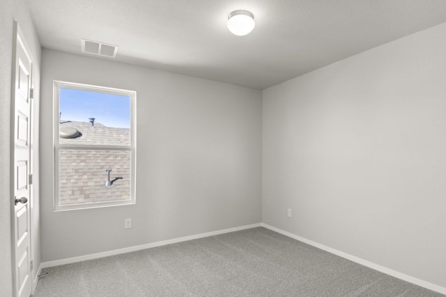 Image of a bedroom with light grey walls, tan carpeting, and a window